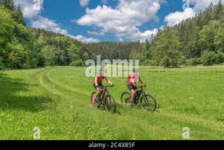 Großmutter mit Elektro-Mountainbike und Enkeltochter ohne elektrische Hilfe auf einem glatten Wiesenweg in der Fränkischen Schweiz bei Bavari Stockfoto