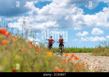 Großmutter und Enkelin unterwegs mit ihren Mountainbikes an einem sonnigen Sommertag zwischen roten Mohnblumen und Kornfeldern unter einem schönen blauen Himmel Stockfoto