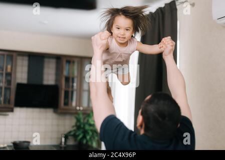 Vater wirft seine geliebte lachende Tochter im Wohnzimmer auf. Stockfoto