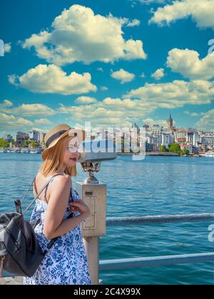 Schöne junge Tourist Mädchen in modischer Kleidung schaut durch Sightseeing binokular zum Galata Tower auf Galata Brücke in Eminonu, Istanbul, Türkei Stockfoto