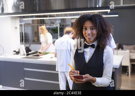 Porträt einer Kellnerin, die in das Notizbuch in der Restaurantküche schreibt Stockfoto