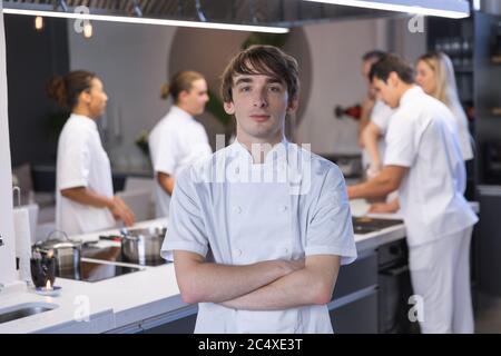 Portrait eines jungen Chefkochs, der mit gekreuzten Armen in der Restaurantküche steht Stockfoto