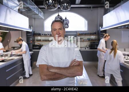 Portrait eines älteren männlichen Küchenchefs, der mit gekreuzten Armen in der Restaurantküche steht Stockfoto