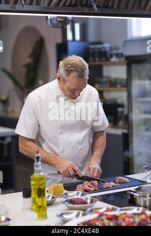 Leitender männlicher Koch, der Fleisch in der Restaurantküche schneidet Stockfoto