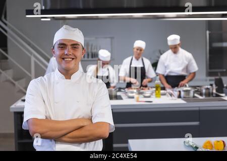 Portrait eines jungen Chefkochs, der mit gekreuzten Armen in der Restaurantküche steht Stockfoto
