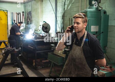 Männliche Fabrik trägt Schürze im Gespräch auf einem Smartphone in der Fabrik Stockfoto