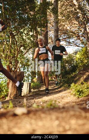 Frau Läuferin läuft auf dem Bergweg mit einem männlichen Athleten hinter ihr. Teilnehmer an einem Cross Country Marathon. Stockfoto