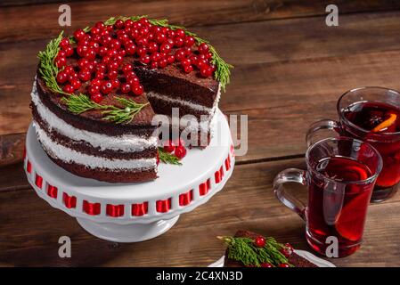 Schöner leckerer Kuchen mit leuchtend roten Beeren auf dem Weihnachtstisch mit duftendem Glühwein mit Gewürzen Stockfoto