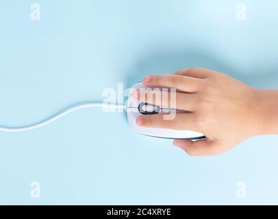 Die Hand des Kindes hält eine Computermaus auf einem blauen Hintergrund. Stockfoto