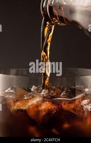 Sekt kohlensäurehaltige Softdrink Cola wird in ein Glas aus einer Flasche gegossen. Schöne Textur von Eis und Blasen close-up in einem Glas Schaum. Stockfoto