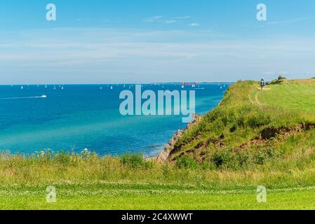 An der Kieler Bucht ein Wanderweg an der Steilküste bei Stohl mit herrlichem Blick auf den Kieler Leuchtturm und die in der Ostsee segelnden Segelboot Stockfoto