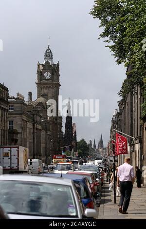 Princes Street, Edinburgh mit Autoverkehr, dem legendären Balmoral Hotel und dem Scott Monument im Hintergrund. Fußgänger und Touristen, die auf dem Bürgersteig laufen. Stockfoto