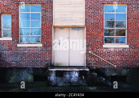 Ein verlassene Lagerhaus Gebäude Eingang mit Fenstern und Tür Gasse Laden Dock mit alten Moos Backstein Fundament Stockfoto