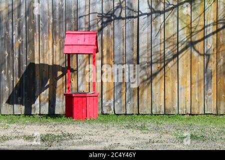 Ein sehr leuchtend roter Wunschwasserbrunnen vor einem braunen Zaun und Gras Stockfoto