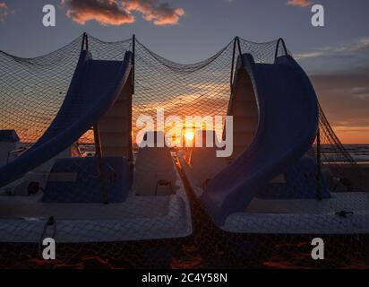 Sonnenstrahlen, die sich auf Tretbooten spiegeln, die mit Fischernetzen bedeckt sind, am Morgen während des wunderschönen Sonnenaufgangs am Strand von Rivazzurra (Rimini/Italien) Stockfoto