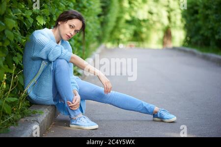 Hübsches Mädchen trägt blaue Jeans, Turnschuhe und Strickpullover. Im Freien Porträt einer schönen Frau im Stadtpark Stockfoto