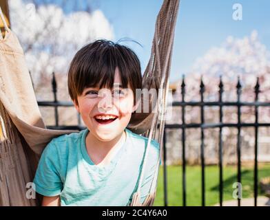 Glücklicher Junge, der an einem Sommertag in einer Hängematte in einem Hinterhof sitzt. Stockfoto
