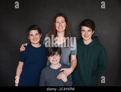 Porträt der Mutter mit drei älteren Jungen vor schwarzem Hintergrund. Stockfoto