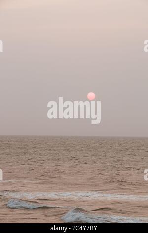 Ein Vollmond taucht am Horizont auf, während die Wellen brechen Auf der Meeresoberfläche Stockfoto