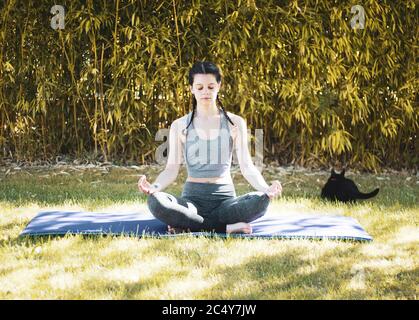 Junge Mädchen tun Yoga im Garten mit Matte und Eine Katze Stockfoto