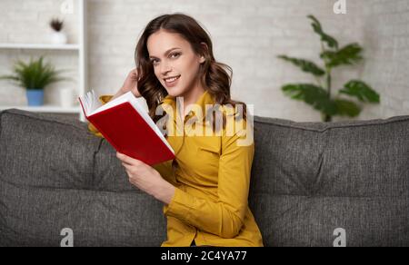 Mädchen sitzt auf einem Sofa und liest zu Hause ein Buch Stockfoto