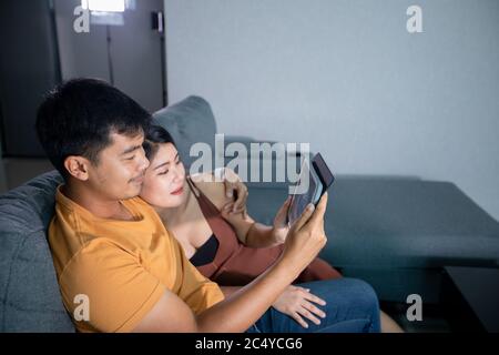 Asiatische schöne schwangere Frau und Mann suchen Ultraschall-Scan auf einer Couch im Wohnzimmer zu Hause. Konzept der Schwangerschaft Gesundheitsversorgung. Stockfoto