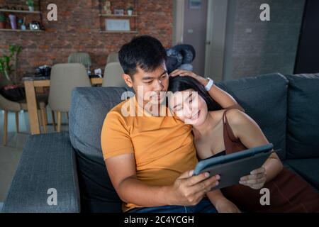 Asiatische schöne schwangere Frau und Mann suchen Ultraschall-Scan auf einer Couch im Wohnzimmer zu Hause. Konzept der Schwangerschaft Gesundheitsversorgung. Stockfoto