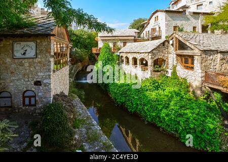 Malerische mittelalterliche Steingebäude beherbergen Cafés und Restaurants mit Terrassen in der Nähe des Flusses Neretva in Mostar, Bosnien-Herzegowina Stockfoto