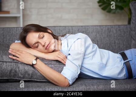 Müde Frau schläft in Kleidung auf einem Sofa zu Hause Stockfoto