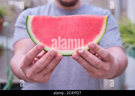 Nicht erkennbarer Mann, der eine kernlose Wassermelonenscheibe anbietet. Obst, Sommerkonzept. Stockfoto
