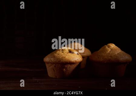 Drei hausgemachte Muffins Cupcake liegt auf altem Buch auf schwarzem Hintergrund Stockfoto