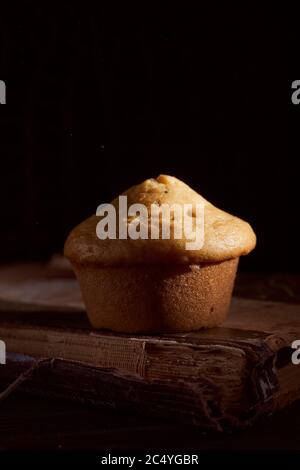 Hausgemachter Muffin Cupcake liegt auf altem Buch auf schwarzem Hintergrund Stockfoto