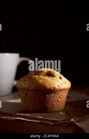 Hausgemachter Muffin Cupcake liegt auf altem Buch auf schwarzem Hintergrund Stockfoto