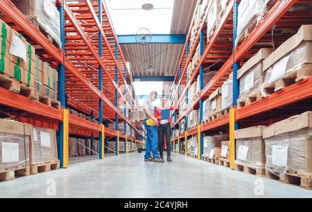 Das Arbeitsteam steht zwischen hohen Regalen im Logistiklager Stockfoto