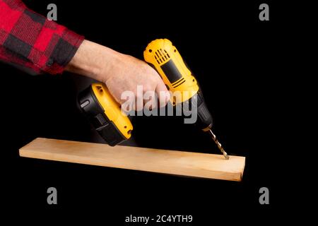 Ein Arbeiter in einem roten karierten Hemd verwendet einen elektrischen Bohrer isoliert auf schwarz Stockfoto