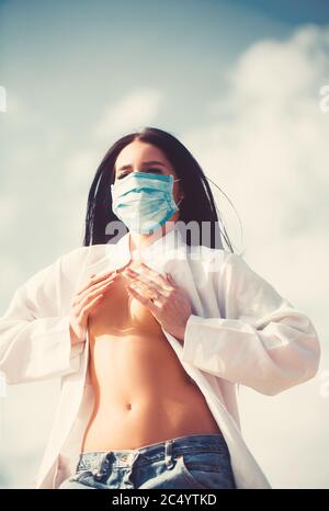 Junge Frau, die sich vor dem Corona Virus schützt, covid 19 mit einer Maske auf blauem Himmel Hintergrund Stockfoto