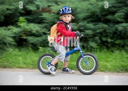 Niedliches Kleinkind Junge mit blauem Helm, Reiten Laufrad auf der Straße, verschwommener Hintergrund Stockfoto