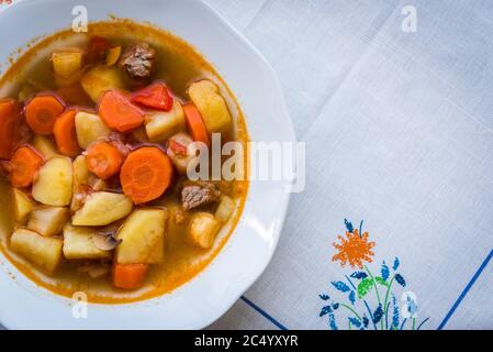 Traditionelle hausgemachte ungarische heiße Gulaschsuppe mit Mem, Kartoffeln, Karotten und Pilzen auf einem weißen Teller auf dem Tisch. Europäische Küche. Draufsicht. Stockfoto