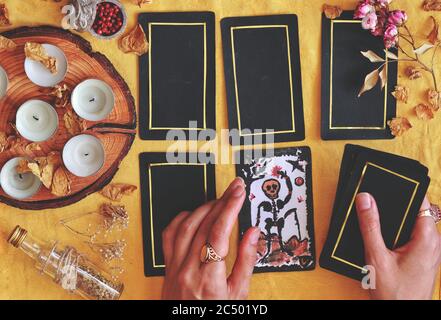 Wiccan Hexe liest die Zukunft auf ihrem Altar mit 5 Karten Tarot auf hellgelben Tuch (flach legen) Hand gemalt Tod Tarot Karte in der Hand halten Stockfoto