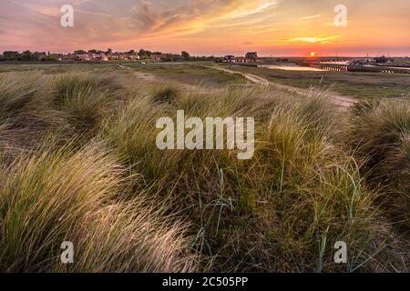 Walberswick, Suffolk, England, Großbritannien bei Sonnenuntergang. Blick über das Marrammgras, das auf den Dünen wächst, mit dem Dorf auf der linken Seite und dem Fluss Blyth auf der rechten Seite. Stockfoto