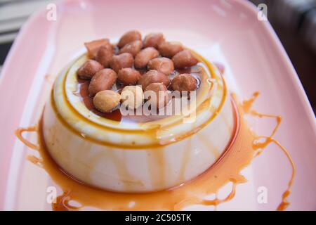 Thailändisches Puddingdessert, hergestellt aus der tropischen Pflanze Pandanus (Pandanus amaryllifolius), serviert mit salzigen Erdnüssen und süßem Sirup auf einem rosa Teller Stockfoto