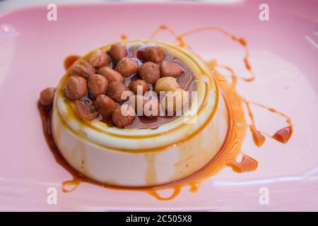 Thailändisches Puddingdessert, hergestellt aus der tropischen Pflanze Pandanus (Pandanus amaryllifolius), serviert mit salzigen Erdnüssen und süßem Sirup auf einem rosa Teller Stockfoto
