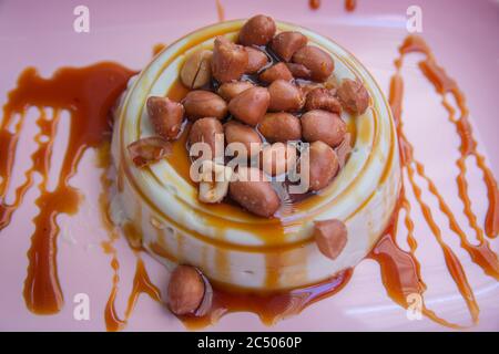 Thailändisches Puddingdessert, hergestellt aus der tropischen Pflanze Pandanus (Pandanus amaryllifolius), serviert mit salzigen Erdnüssen und süßem Sirup auf einem rosa Teller Stockfoto
