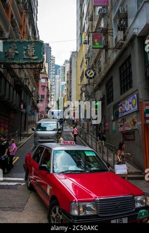 Eine Straßenszene in Central, Hong Kong mit einem roten Taxi, anderen Fahrzeugen und Fußgängern, die von Hochhäusern umgeben sind. Stockfoto