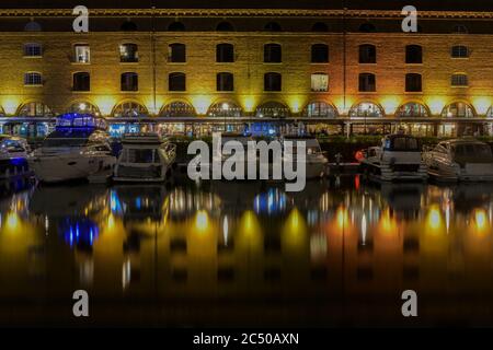 Nachtansicht von St. Katherine Dock Marina in London mit dem Gebäude und den Vergnügungsbooten, die Spiegelung auf dem stillen Wasser werfen. Stockfoto