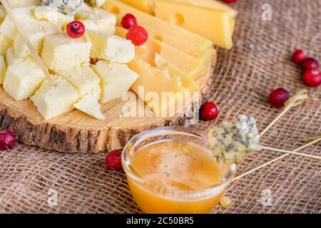 Käsestücke auf natürlichem Hintergrund. Verschiedene Käsesorten auf Holzbrett. Käse mit Schimmel und Honig aus der Nähe, Seitenansicht. Käsescheiben mit Stockfoto