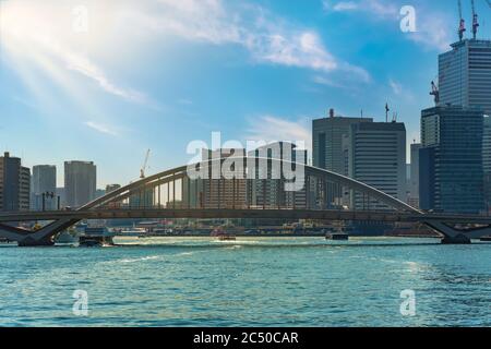 tokio, japan - märz 15 2020: Wasserbusse fahren auf dem Sumida-Fluss unter der Bogenbrücke von Tsukiji Ohashi, die von der Kanni-Straße mit dem Skyscra überquert wird Stockfoto