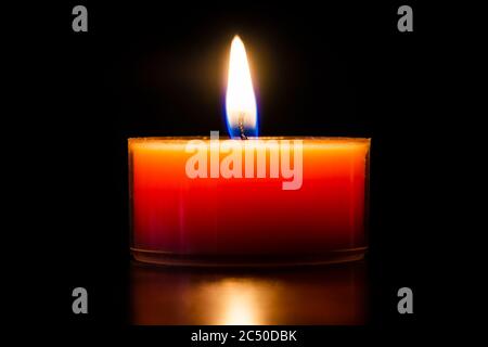 Orange brennende Kerze in einem Glas Teelicht schöne Nahaufnahme isoliert auf schwarz. Stockfoto