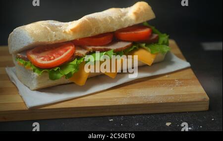 Ein appetitliches Sandwich mit Schinken, Käse, Tomaten und Salat liegt auf einem Brett mit Ei und Zitrone auf schwarzem Hintergrund Stockfoto