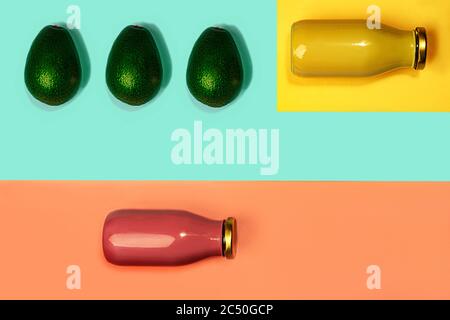 Flaschen mit bunten Säften oder Smoothies und Avocado auf gelbem, pinkfarbenem Korallen und trendigen mintgrün-blauen Hintergrund. Flache Lage, Draufsicht, Nahaufnahme. Minimaler Stil. Stockfoto